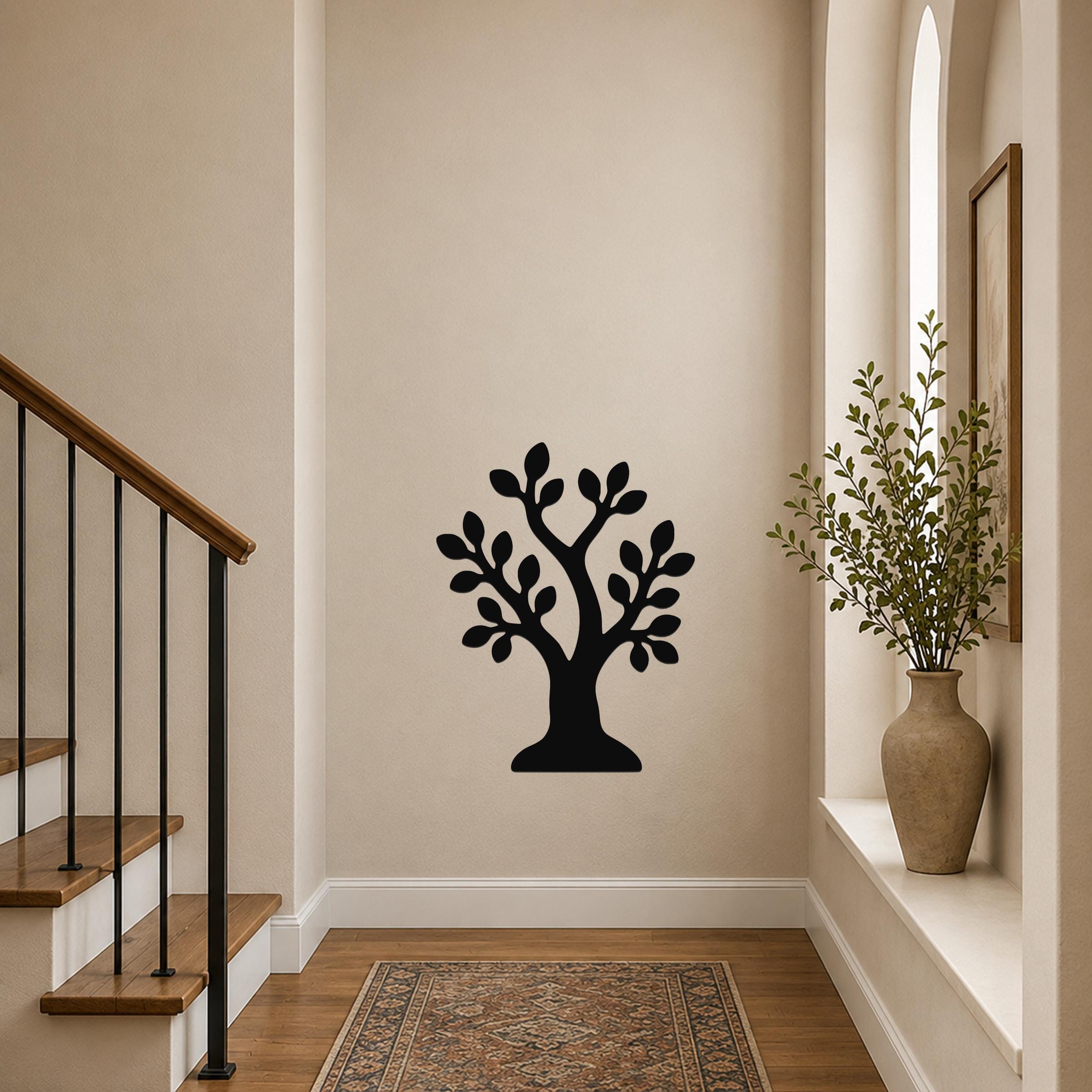 Black metal wall art in the shape of a tree with leaf cutouts, mounted on a hallway wall near a staircase and a window with a vase.