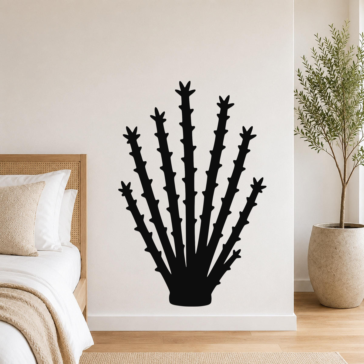 Black metal ocotillo wall art silhouette with spiky branches, mounted on a bedroom wall above a bed.