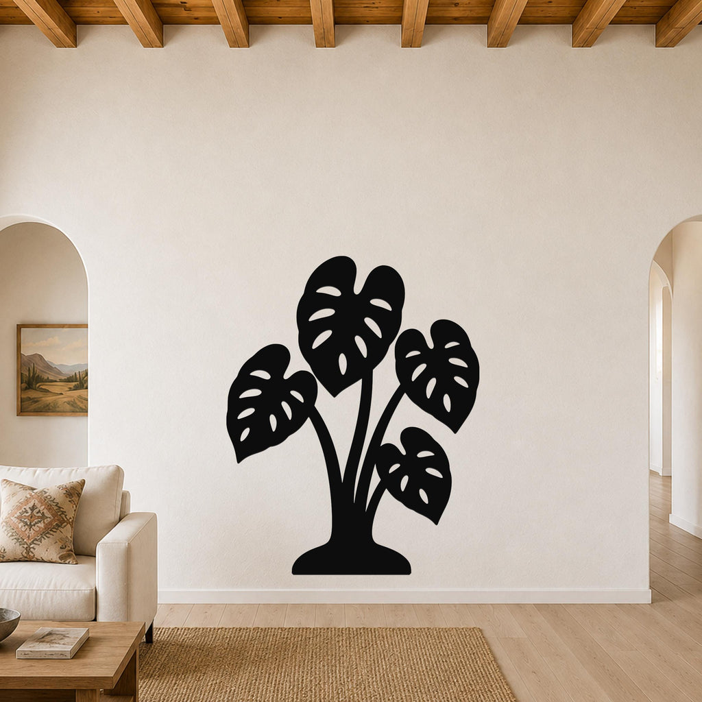 Black metal wall art cutout of a monstera plant with leaf perforations, mounted on a living room wall above a sofa.