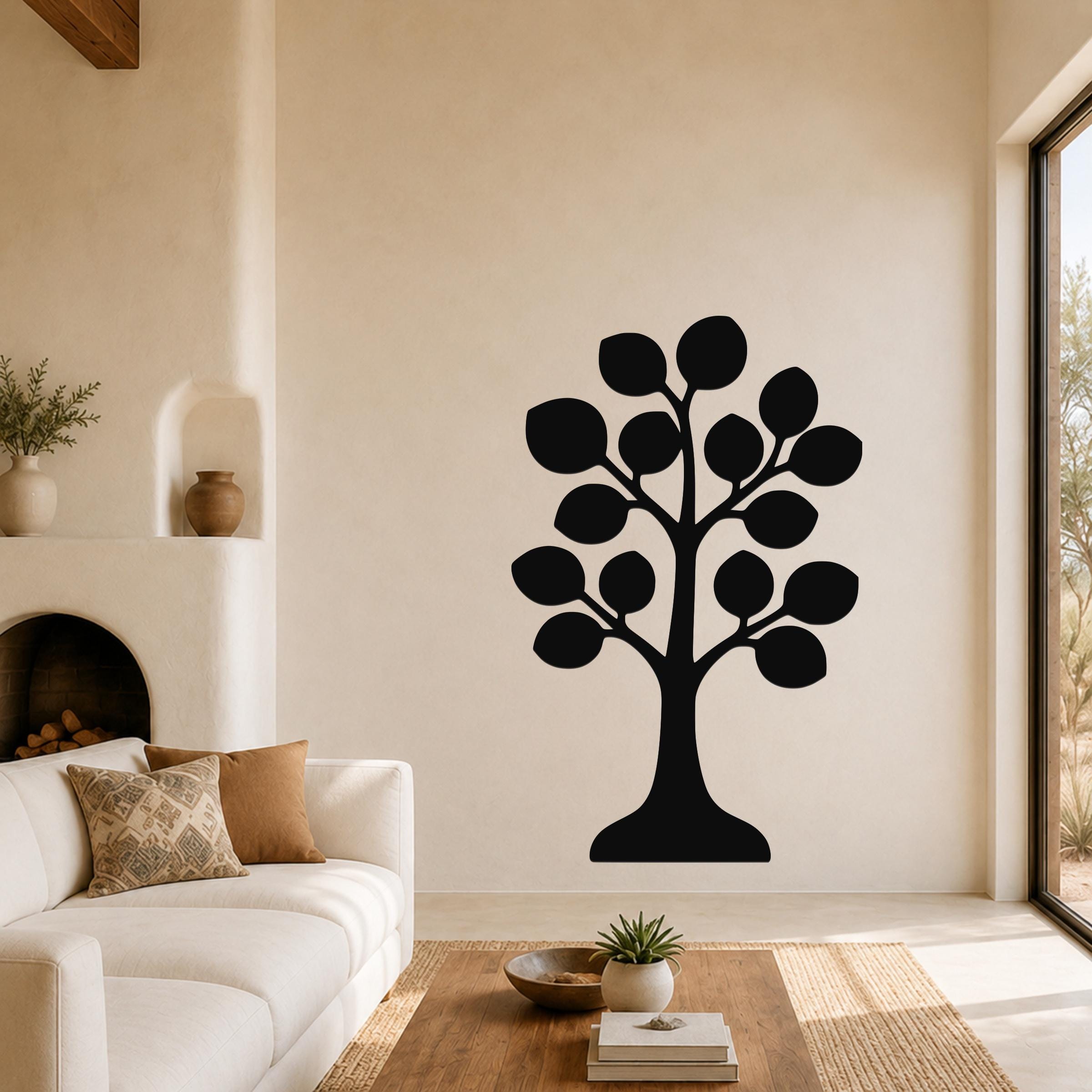 Black metal tree wall art with leaf cutouts, mounted on a living room wall above a sofa.
