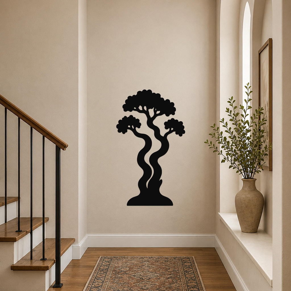 Black metal wall art in a bonsai tree silhouette with wavy trunks and layered canopy, mounted on a hallway wall above a patterned rug near a staircase.