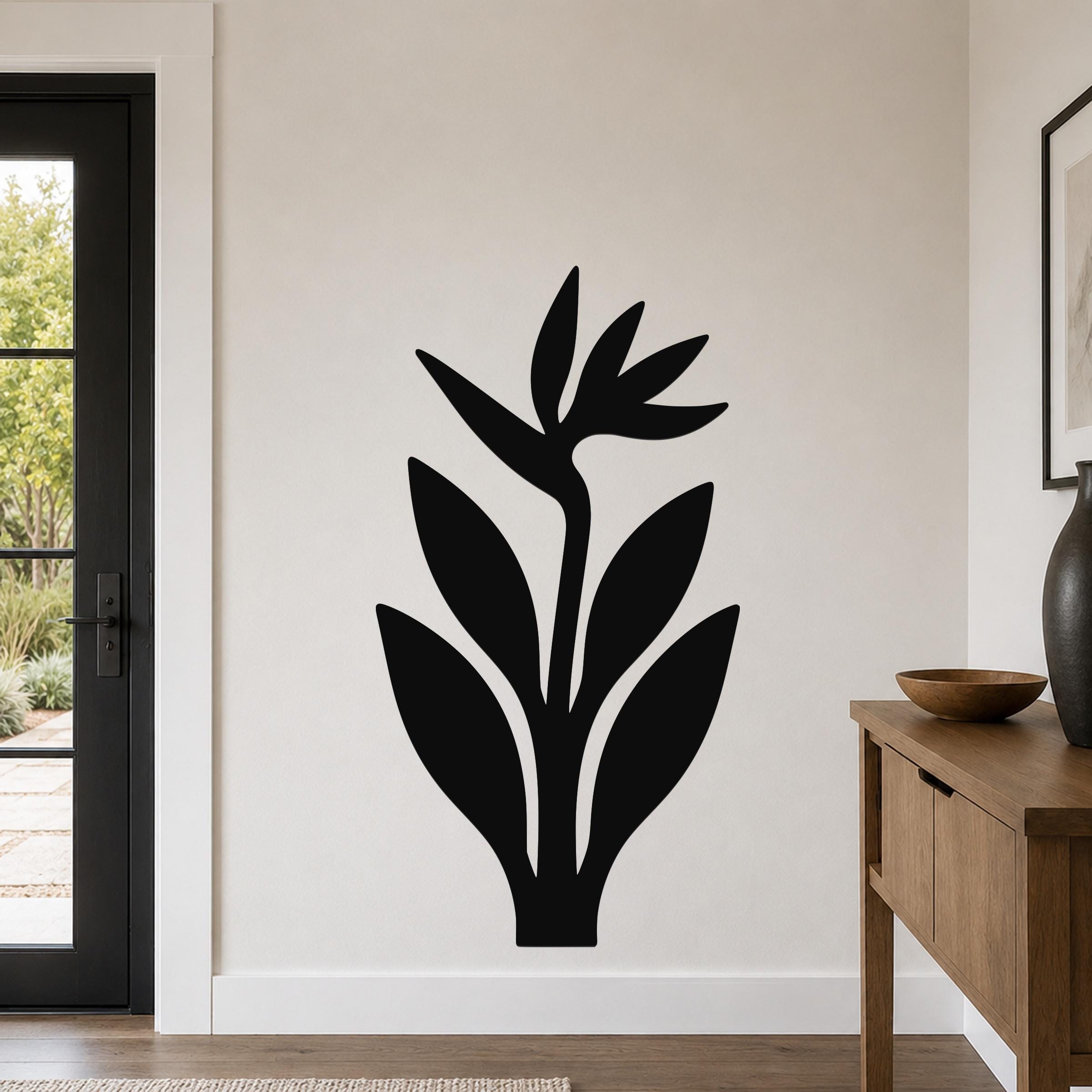 Black metal Bird of Paradise wall art with leaf and flower cutouts, mounted on a light-colored wall in a modern entryway.