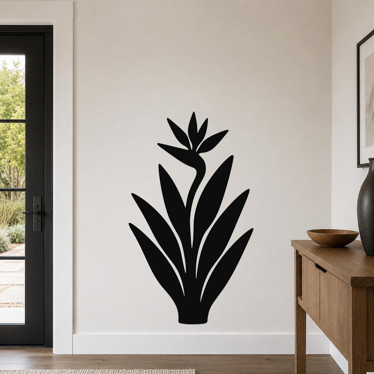 Black metal Bird of Paradise wall art with a silhouette cutout of the flower and leaves, mounted on a light-colored wall in a modern entryway.