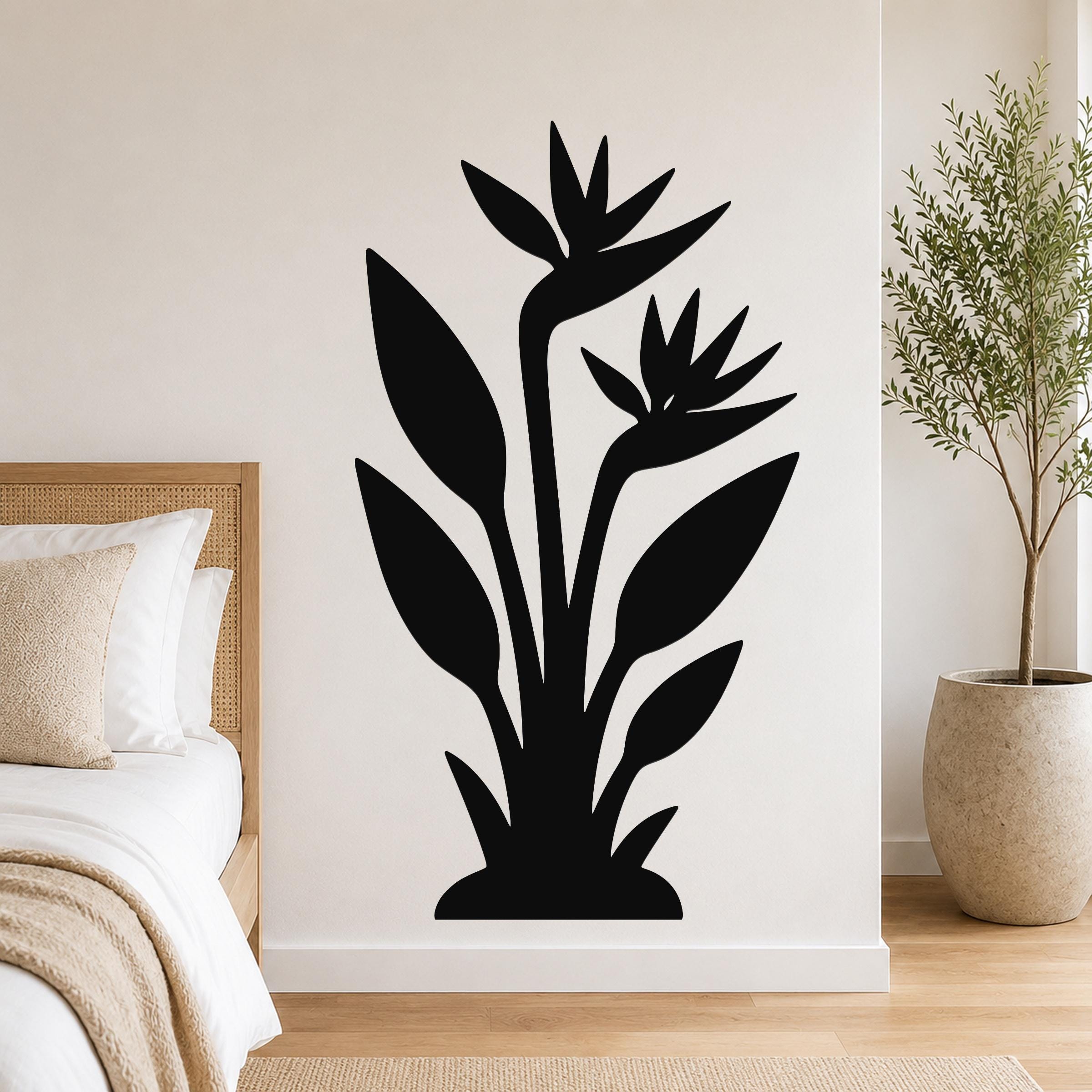 Black metal wall art silhouette of a bird of paradise plant with two flowers and long leaves, mounted on a bedroom wall above a bed.