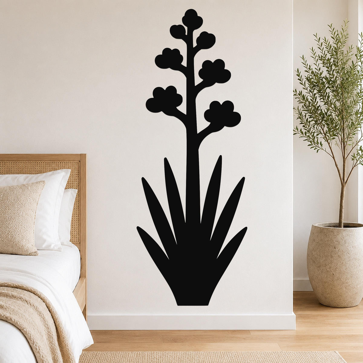 Black metal agave wall art with blooming flower silhouette, mounted on a bedroom wall above a bed.