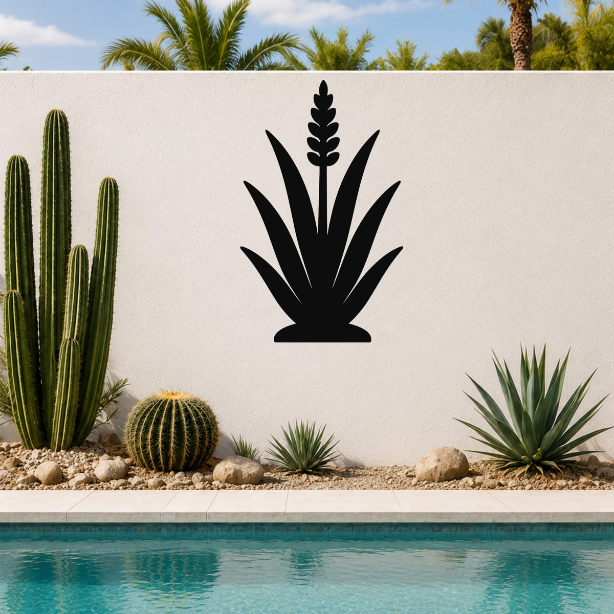 Black metal agave wall art with a tall flower spike cutout, mounted on a white outdoor wall above a poolside garden.