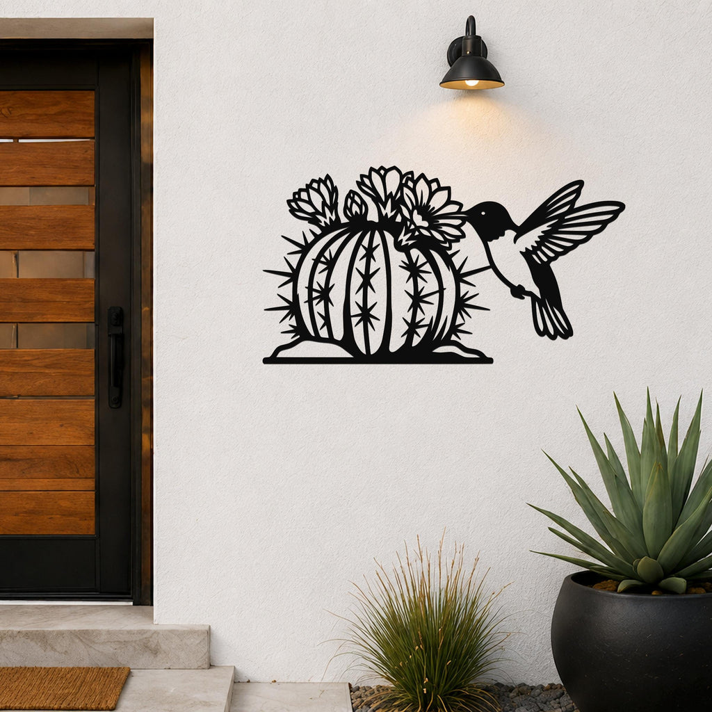 Black metal wall art featuring a hummingbird and flowering barrel cactus cutout, mounted on a white exterior wall beside a front door.