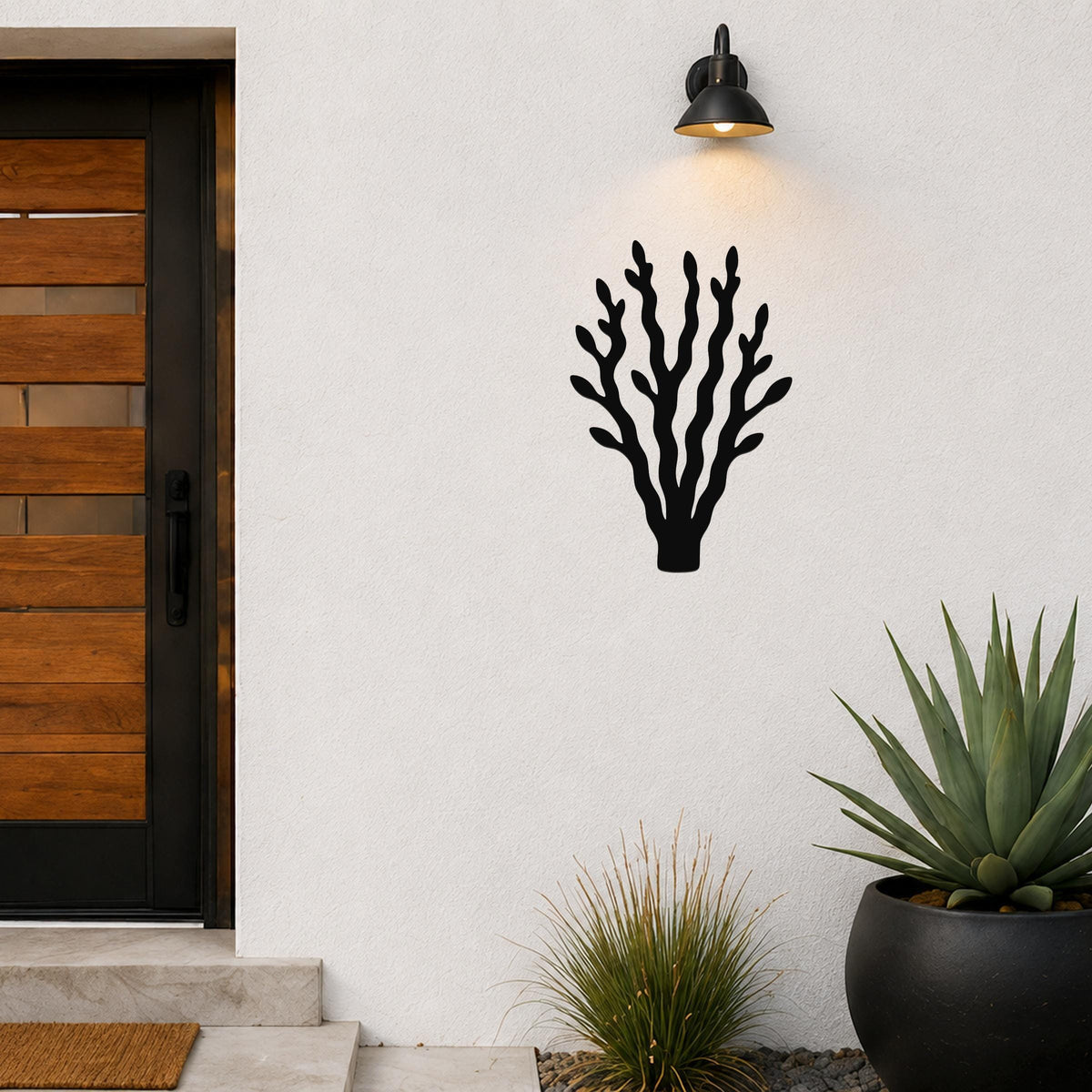 Black metal kelp wall art with branching cutouts, mounted on a white exterior wall above a potted succulent near a front door.