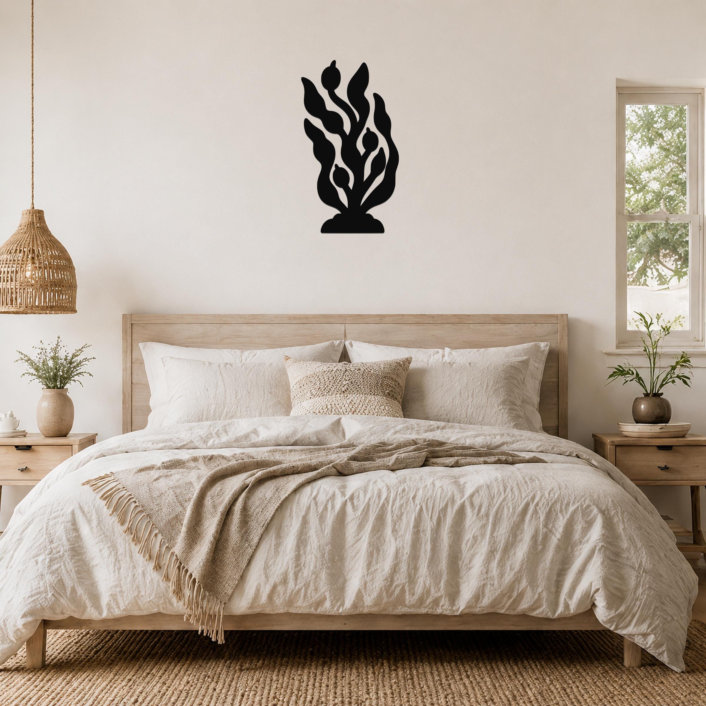 Black metal kelp and seaweed wall art with leafy cutouts, mounted above a wooden bed in a neutral bedroom.