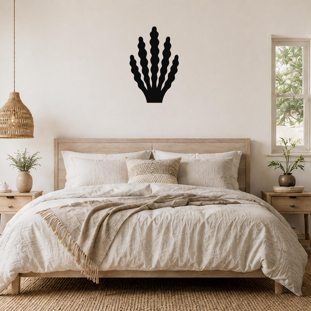 Black metal kelp wall art with wavy frond cutouts, mounted above a wooden bed in a coastal bedroom.