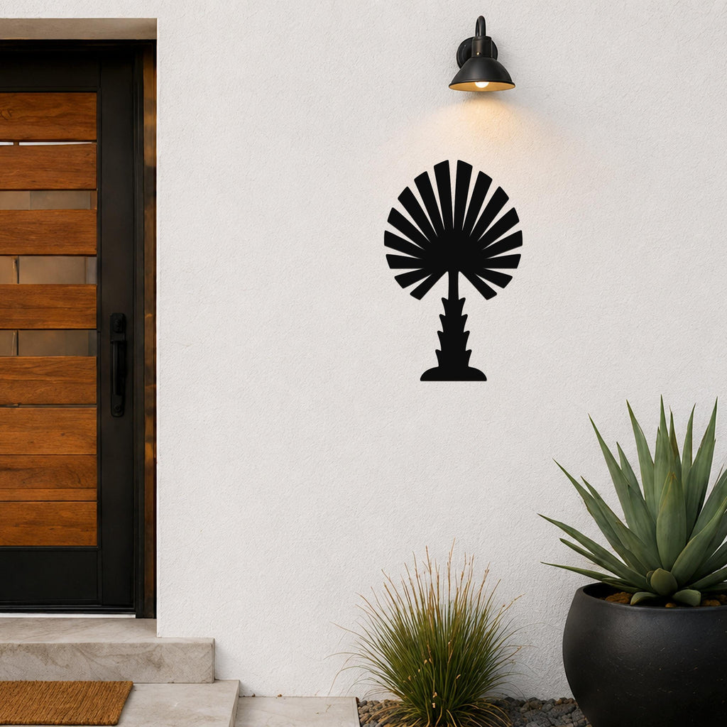 Black metal palm tree wall art with fan-shaped fronds, mounted on a white exterior wall above a potted succulent and near a wooden front door.