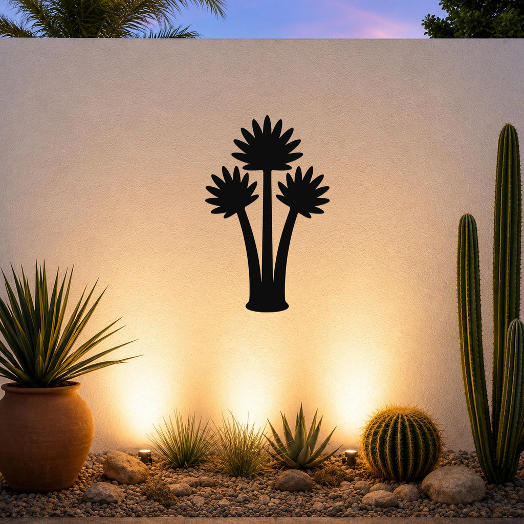 Black metal fan palm tree wall art silhouette mounted on a textured outdoor wall above a desert garden with cacti and warm uplighting.