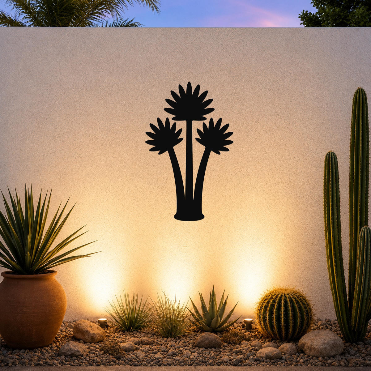 Black metal fan palm tree wall art silhouette mounted on a textured outdoor wall above a desert garden with cacti and warm uplighting.