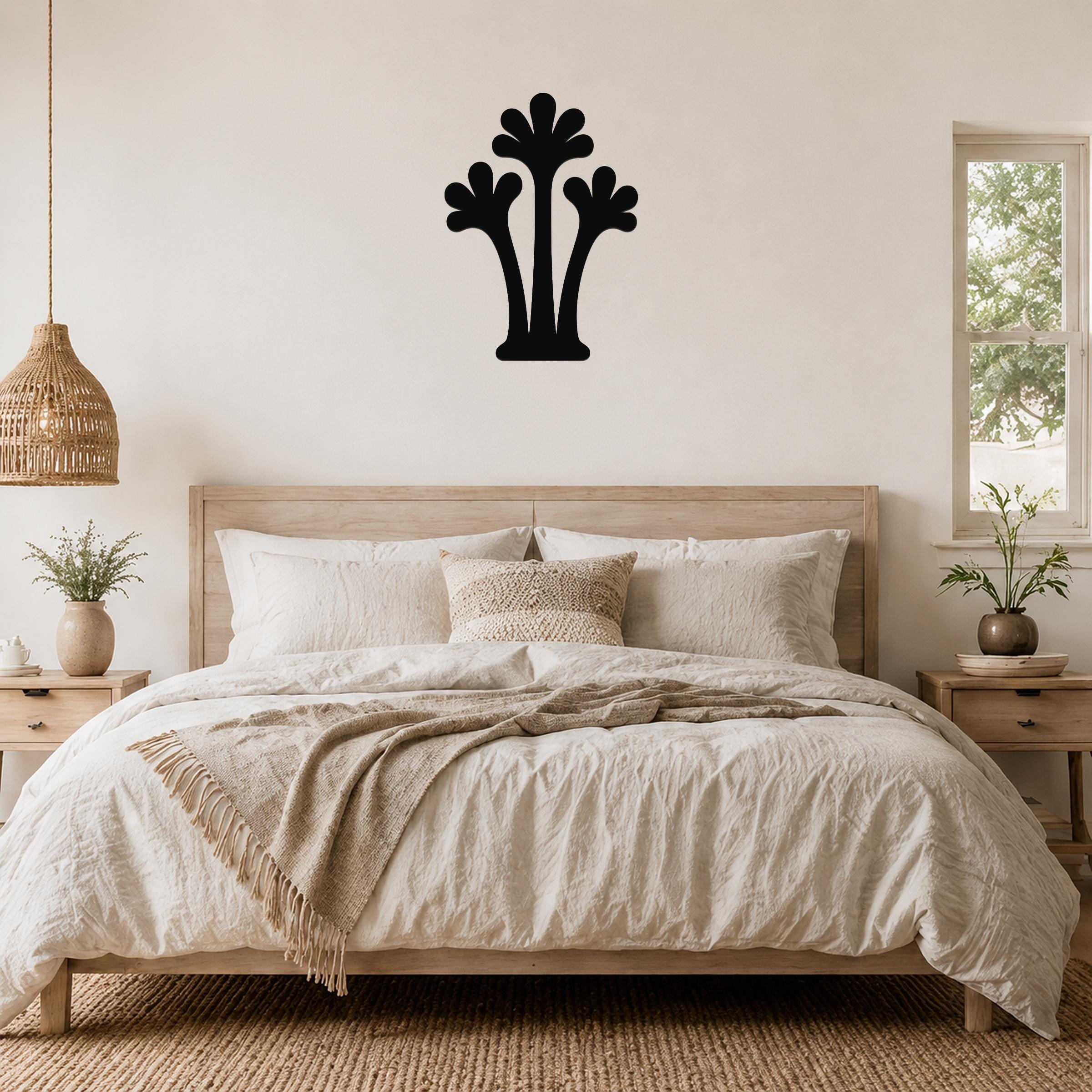 Black metal palm tree wall art with three fronded silhouettes, mounted above a wooden bed in a neutral bedroom.