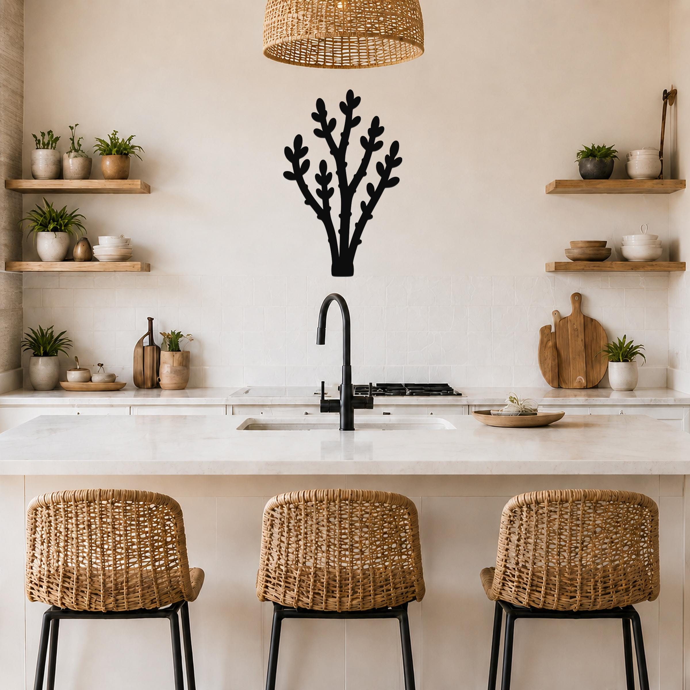 Black metal wall art in a desert branch silhouette, mounted on a kitchen wall above a counter with open shelves and a woven pendant light.