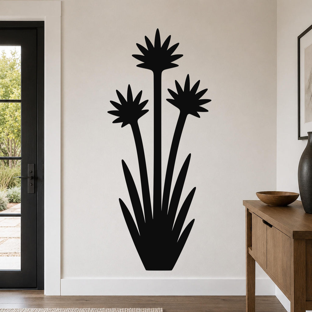 Black metal wall art in a yucca plant silhouette with three starburst flowers and long spiky leaves, mounted on a light-colored wall in a modern entryway.