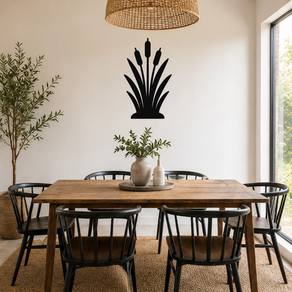 Black metal cattail wall art silhouette with three seed heads and leafy base, mounted on a white wall above a wooden dining table in a bright dining room.