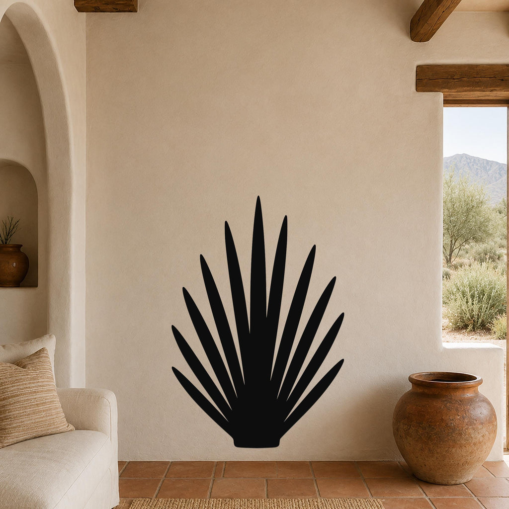 Black metal wall art in a fan-shaped agave silhouette, mounted on a beige stucco wall in a living room with terracotta flooring and wooden beams.