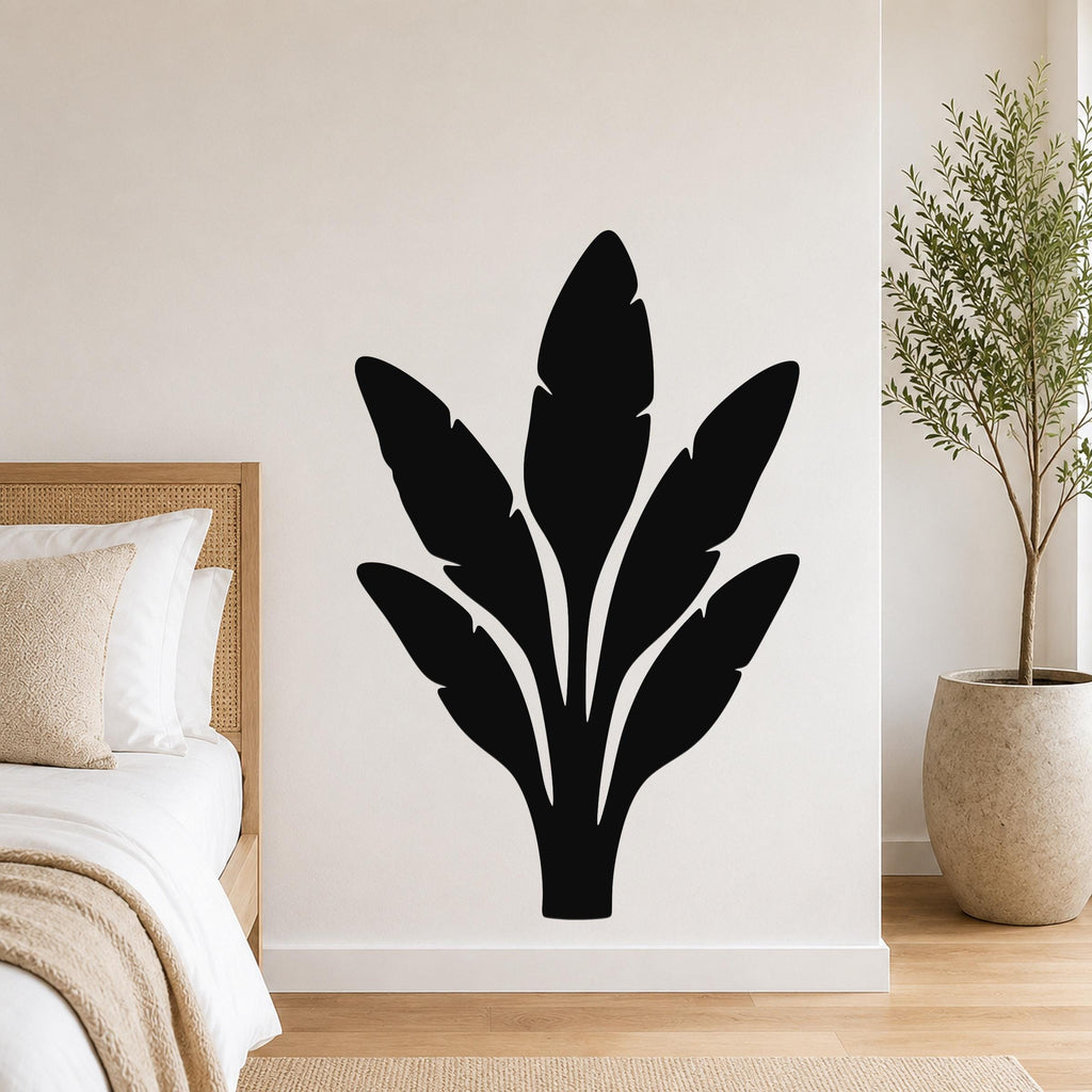 Black metal wall art in a bold banana plant silhouette with layered leaf cutouts, mounted on a bedroom wall above a bed.
