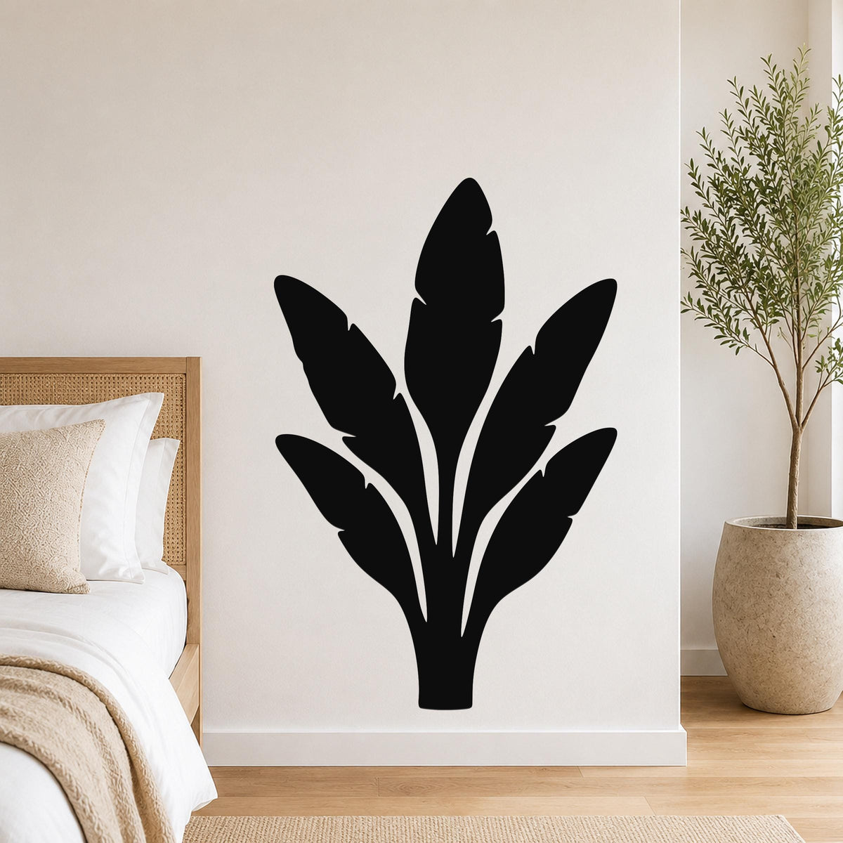 Black metal wall art in a bold banana plant silhouette with layered leaf cutouts, mounted on a bedroom wall above a bed.