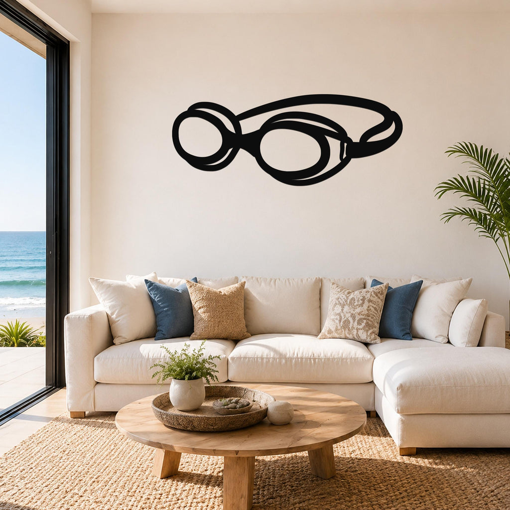 Black metal swim goggles wall art with cutout design, mounted above a white sofa in a living room with ocean views.