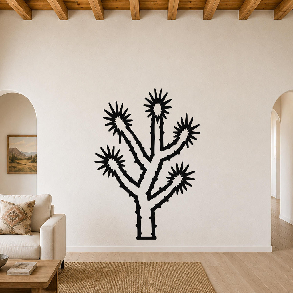 Black metal Joshua tree wall art with spiky branch cutouts, mounted on a living room wall above a sofa.