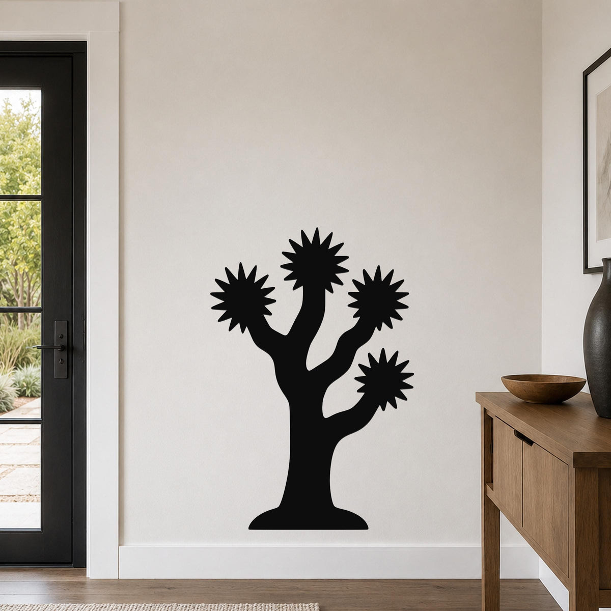 Black metal Joshua tree wall art with starburst-shaped branches, mounted on a white wall in a living room.