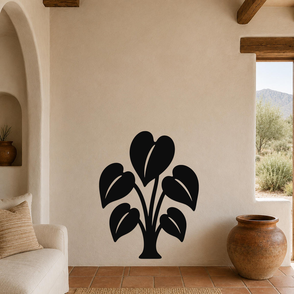 Black metal wall art in the shape of an elephant ear plant with leaf cutouts, mounted on a beige stucco wall in a living room with terracotta flooring and wooden beams.