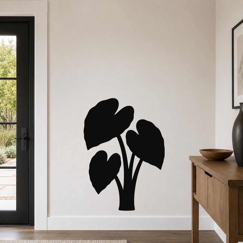 Black metal wall art in the silhouette of an elephant ear plant, mounted on a light-colored wall in a living room near a door and console table.