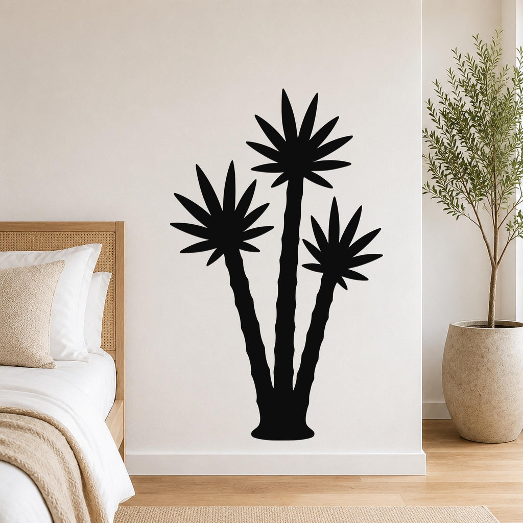 Black metal wall art featuring a silhouette of three abstract palm trees, mounted on a bedroom wall above a bed.