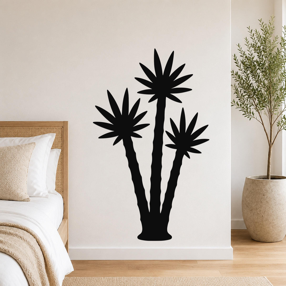 Black metal wall art featuring a silhouette of three abstract palm trees, mounted on a bedroom wall above a bed.