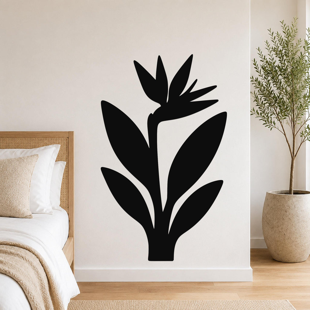 Black metal wall art in a Bird of Paradise silhouette, mounted on a white bedroom wall above a bed with a woven headboard.