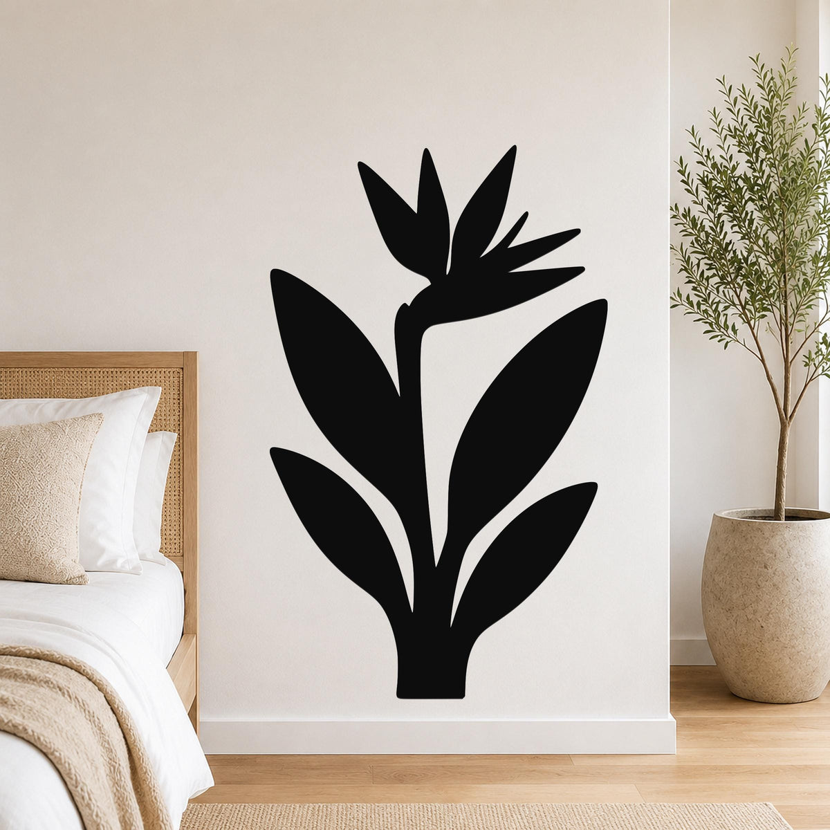 Black metal wall art in a Bird of Paradise silhouette, mounted on a white bedroom wall above a bed with a woven headboard.