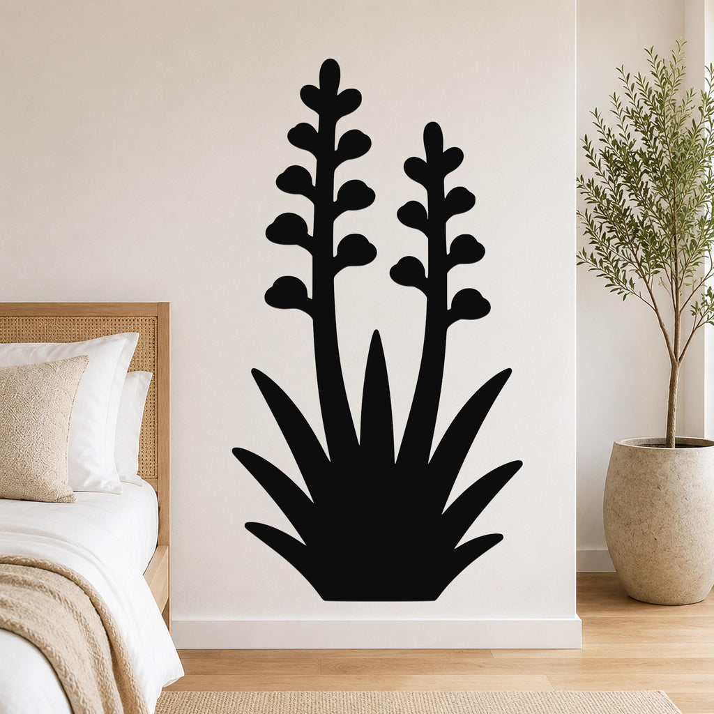 Black metal wall art in a silhouetted agave plant shape with two tall flower stalks, mounted on a bedroom wall above a bed.