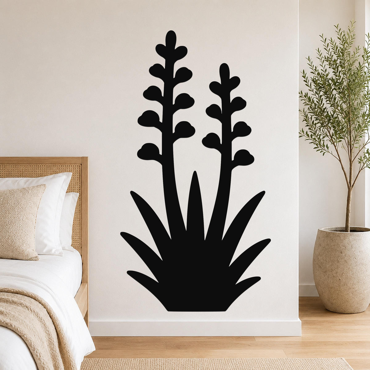 Black metal wall art in a silhouetted agave plant shape with two tall flower stalks, mounted on a bedroom wall above a bed.