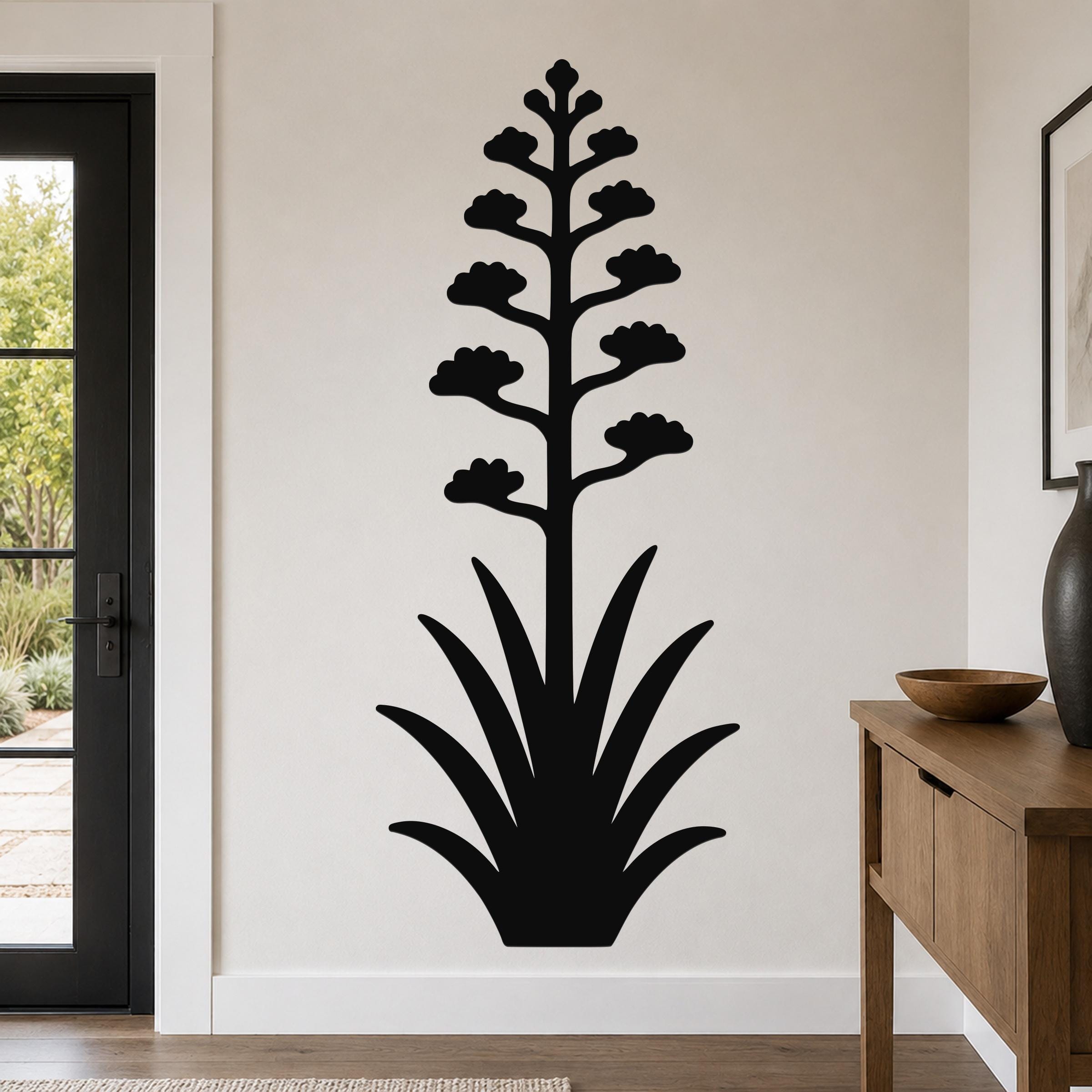 Black metal wall art in the silhouette of a blooming agave plant with a tall flower stalk and spiky leaves, mounted on a living room wall above a wooden console table.