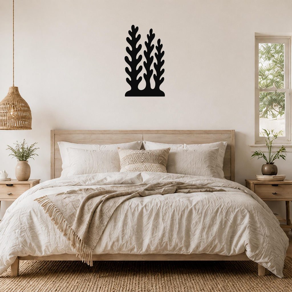 Black metal wall art with a kelp or seaweed silhouette design, mounted above a wooden bed in a neutral bedroom.