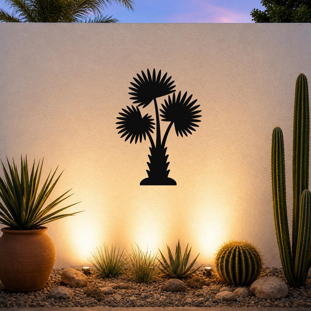 Black metal palm tree wall art with fan-shaped fronds and a textured trunk, mounted on an outdoor wall above a desert garden with cacti and warm uplighting.