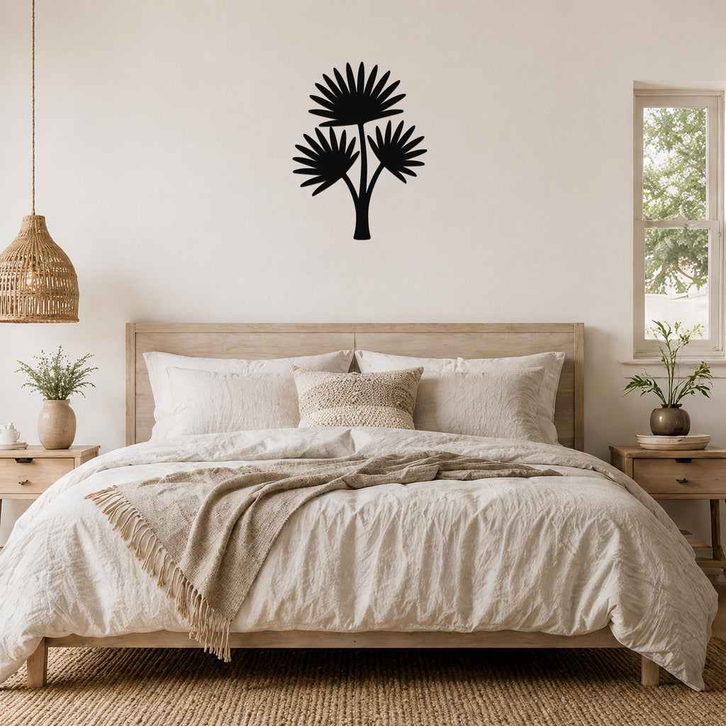 Black metal cutout wall art of a fan palm tree with three fronds, mounted on a wall above a bed in a neutral bedroom.