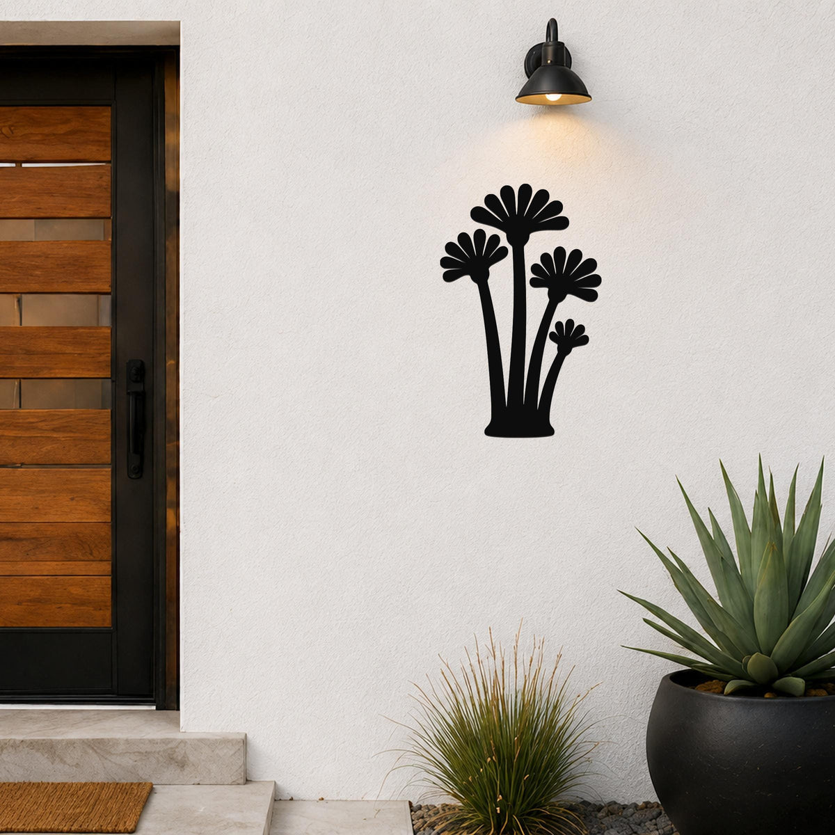 Black metal wall art with a fan palm tree silhouette, mounted on an outdoor wall beside a wooden door and potted plants.