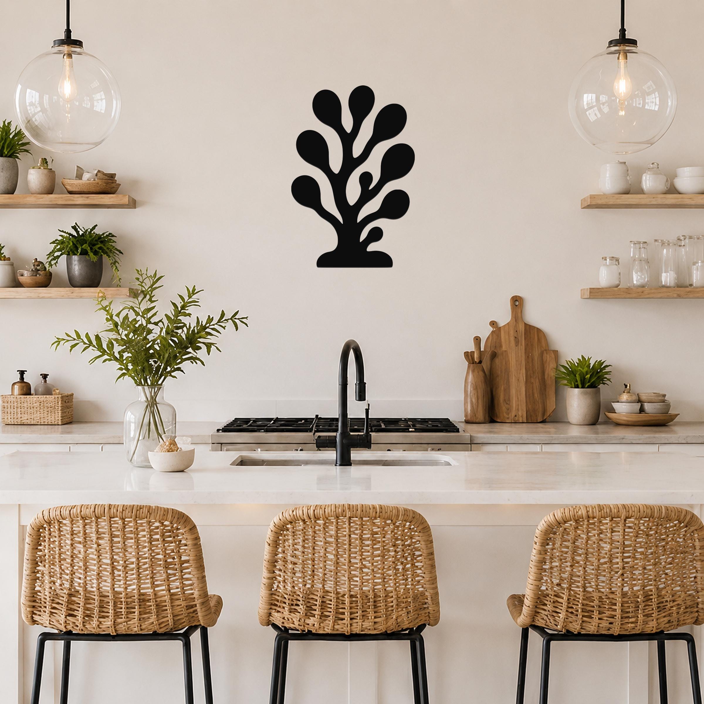 Black metal coral wall art with branching cutouts, mounted on a kitchen wall above a counter between two glass pendant lights.