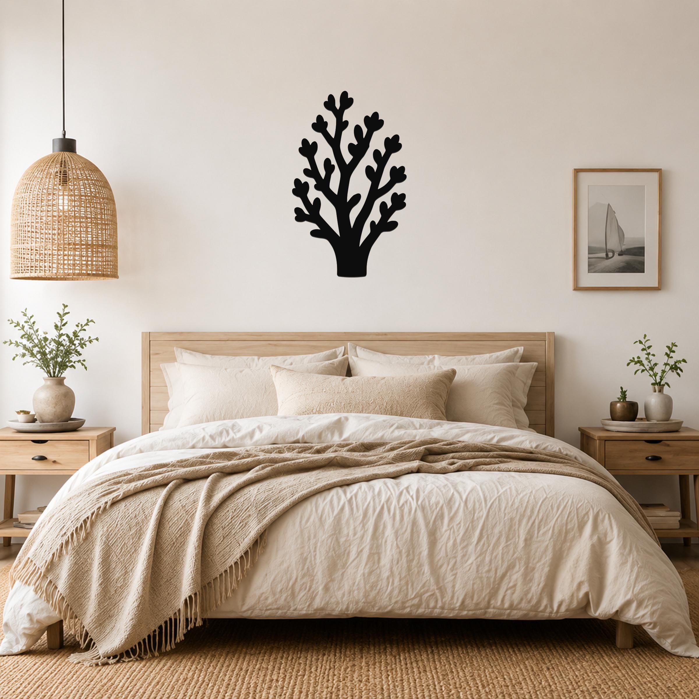 Black metal wall art in a tree silhouette with branching cutouts, mounted above a wooden bed in a neutral bedroom.