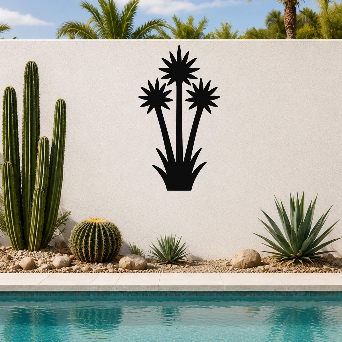 Black metal wall art cutout of a blooming yucca plant with three starburst flowers and spiky base, mounted on a white outdoor wall above a poolside garden.