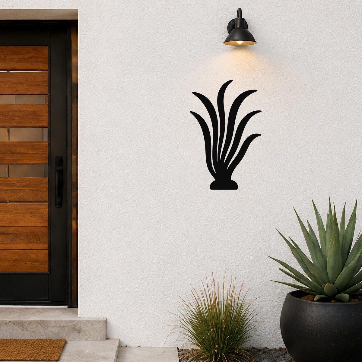 Black metal kelp wall art with flowing leaf cutouts, mounted on a white exterior wall above a potted succulent and near a modern front door.