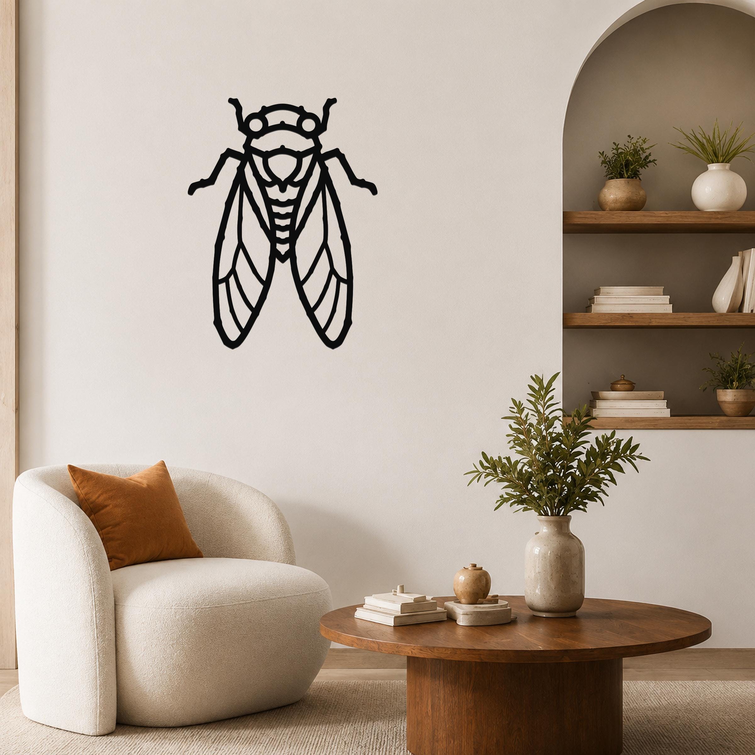 Black metal cicada wall art with detailed wing cutouts, mounted on a living room wall above a white armchair.