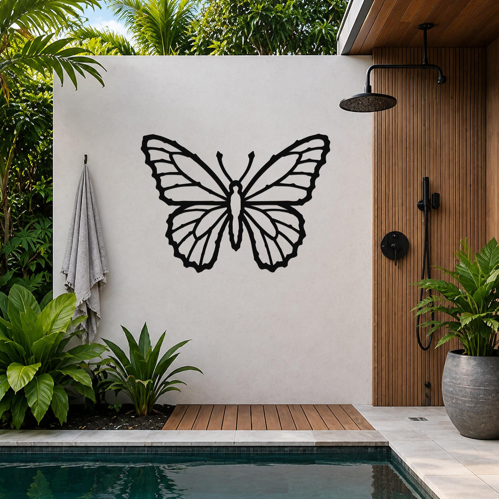 Black metal butterfly wall art with detailed wing cutouts, mounted on a white outdoor wall beside a wooden shower and pool area.