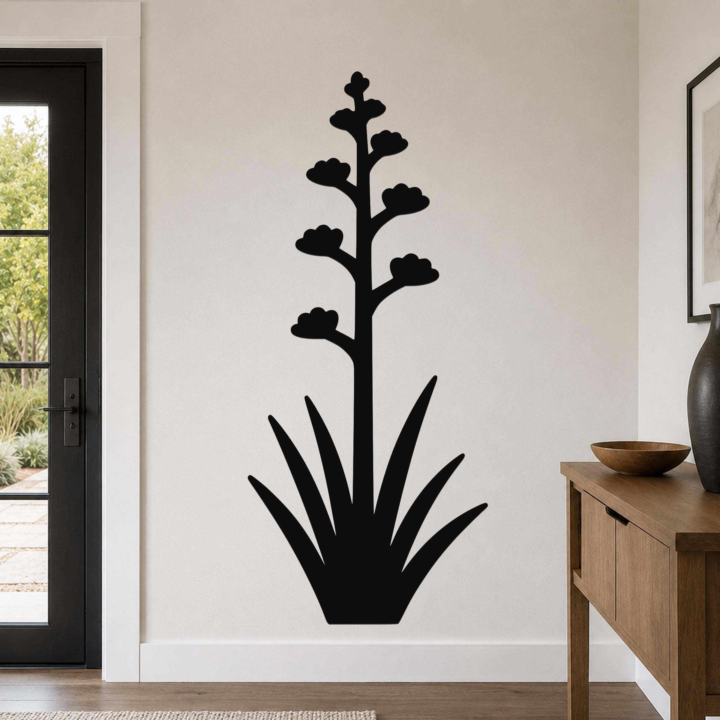 Black metal agave wall art with a tall flowering stalk and spiky leaves, mounted on a living room wall above a wooden console table.