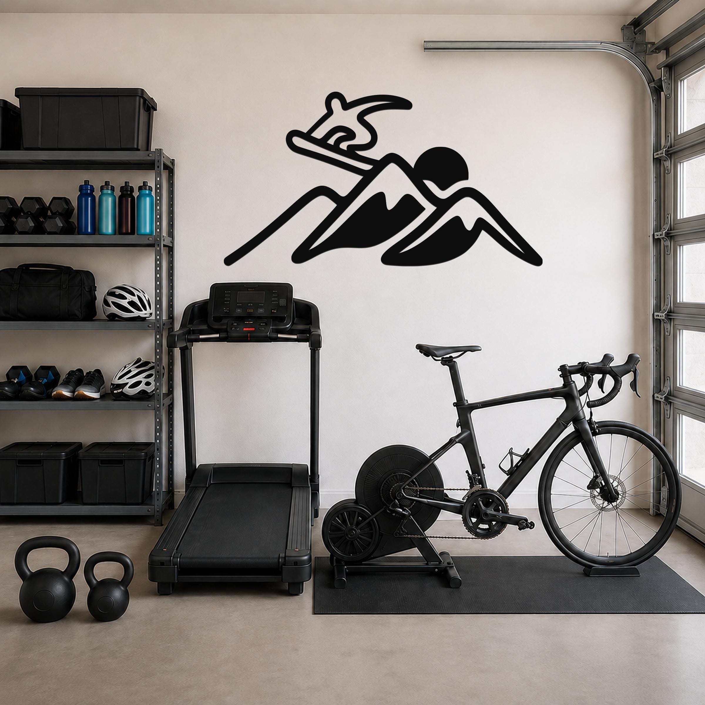 Black metal wall art silhouette of a snowboarder above a mountain, mounted on a garage wall above a treadmill and bicycle.