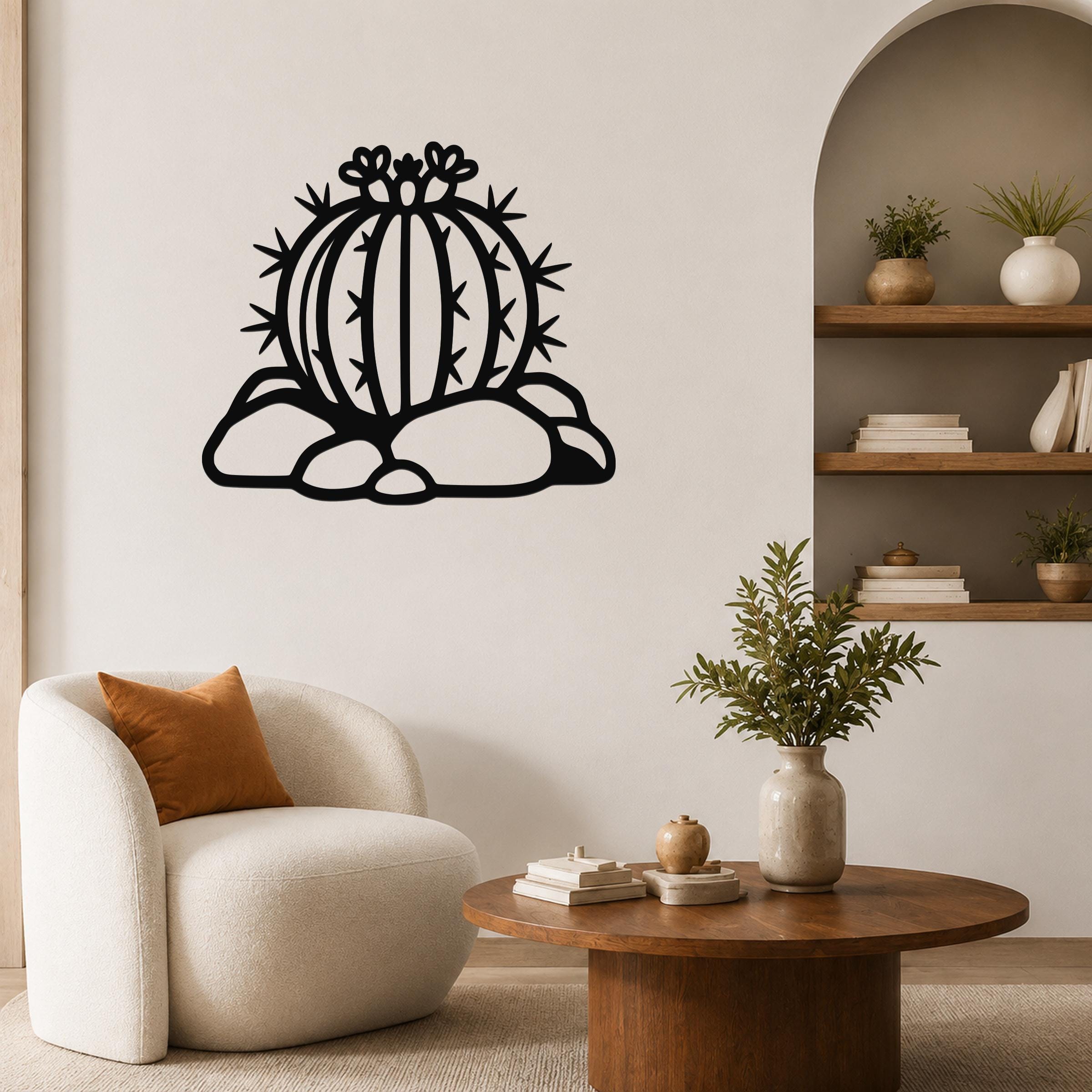 Black metal barrel cactus wall sculpture with flower and spine cutouts, mounted on a living room wall above a white armchair.