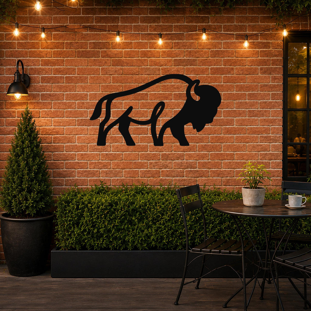 Black metal bison silhouette wall art mounted on a brick patio wall above a planter, with string lights and outdoor furniture in the scene.